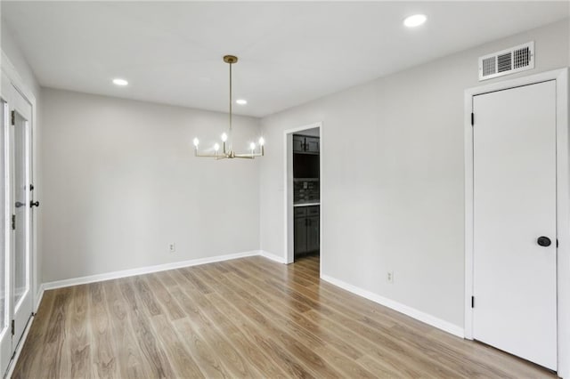 unfurnished room with an inviting chandelier and light hardwood / wood-style flooring