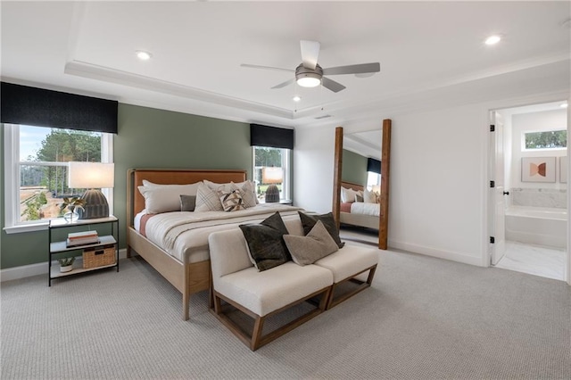 carpeted bedroom with ensuite bathroom, multiple windows, ceiling fan, and a tray ceiling