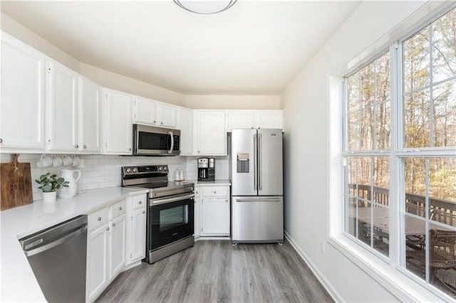 kitchen with tasteful backsplash, white cabinetry, light wood-type flooring, and appliances with stainless steel finishes