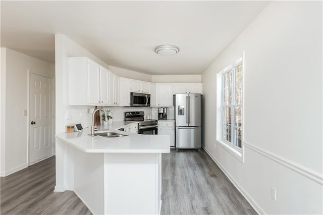 kitchen featuring kitchen peninsula, tasteful backsplash, stainless steel appliances, sink, and white cabinetry