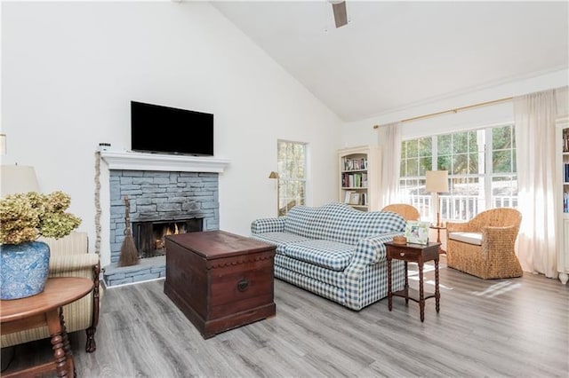 living room featuring ceiling fan, light hardwood / wood-style floors, a stone fireplace, and high vaulted ceiling