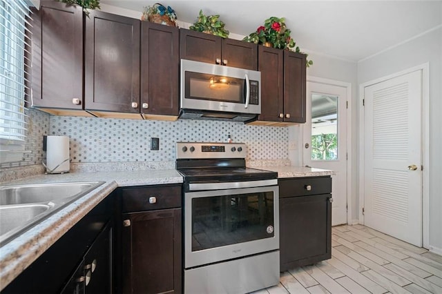 kitchen with light wood-style flooring, dark brown cabinetry, a sink, appliances with stainless steel finishes, and decorative backsplash