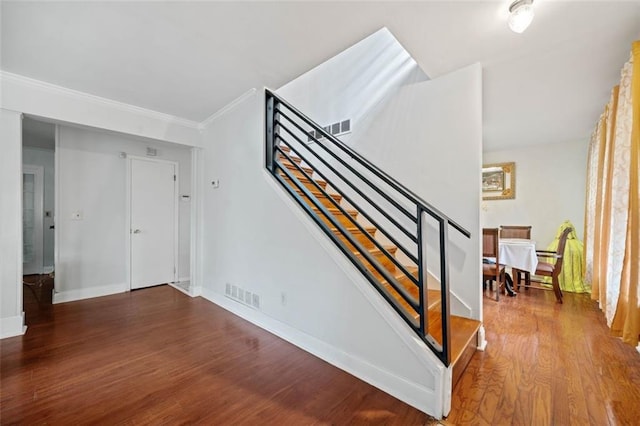 stairs with visible vents, crown molding, baseboards, and wood finished floors