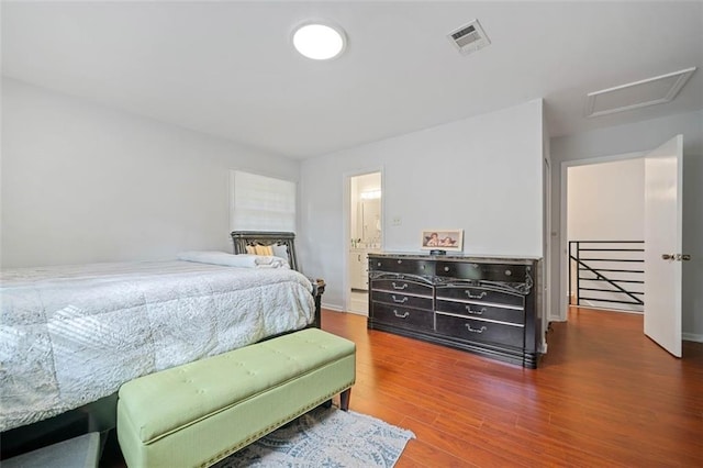 bedroom with dark wood-style floors, visible vents, and attic access