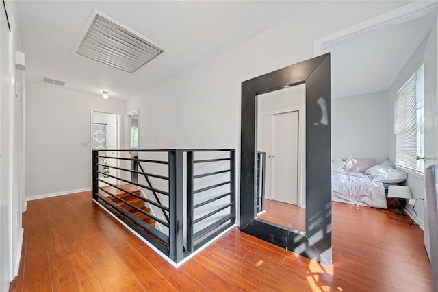 hall with baseboards, visible vents, wood finished floors, and an upstairs landing