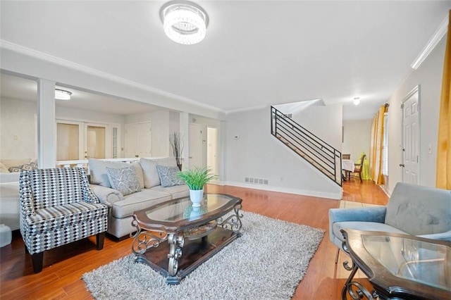 living area with visible vents, baseboards, stairs, light wood finished floors, and crown molding