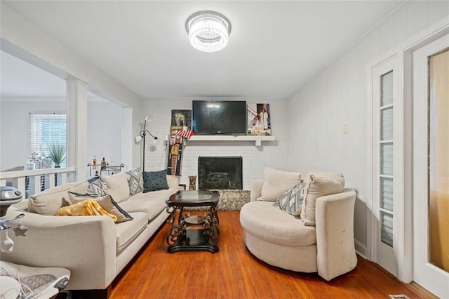 living room with ornamental molding, a fireplace, ornate columns, and wood finished floors