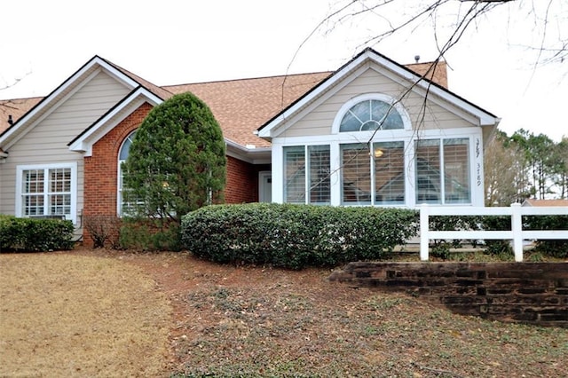 exterior space with brick siding, a shingled roof, and fence