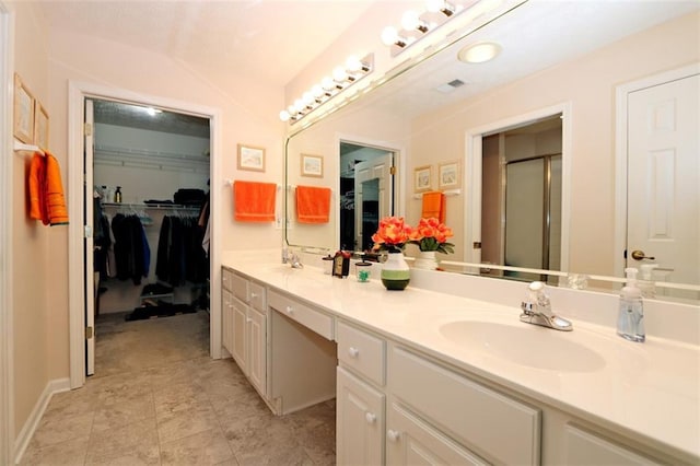 bathroom featuring double vanity, a shower stall, a walk in closet, and a sink