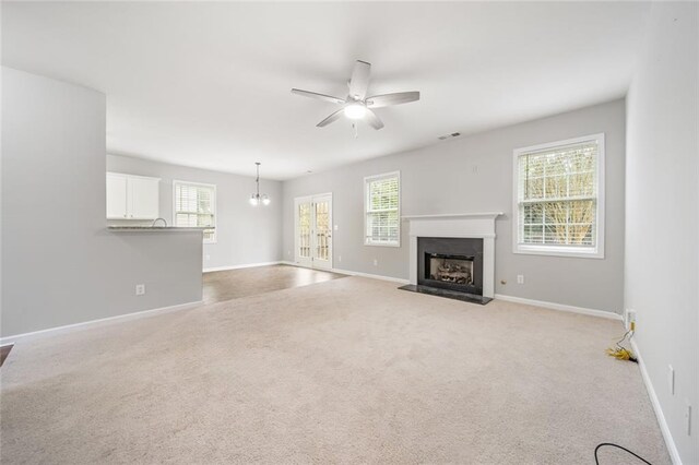 unfurnished living room with light carpet and ceiling fan with notable chandelier