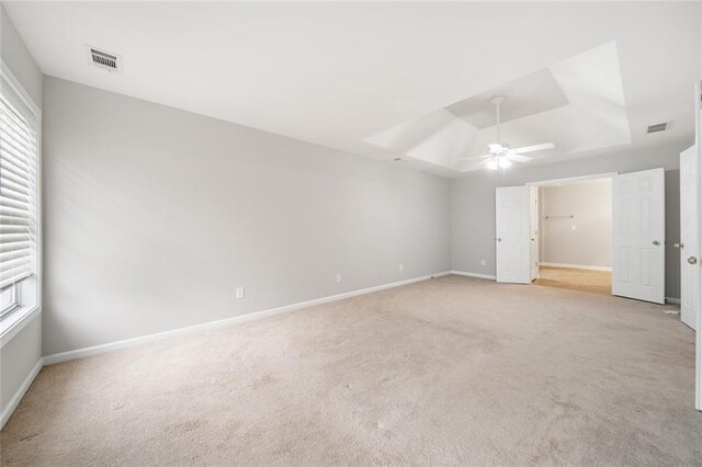 unfurnished bedroom featuring ceiling fan, a raised ceiling, and light carpet