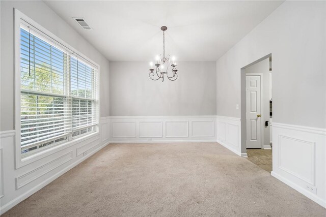 carpeted empty room with an inviting chandelier