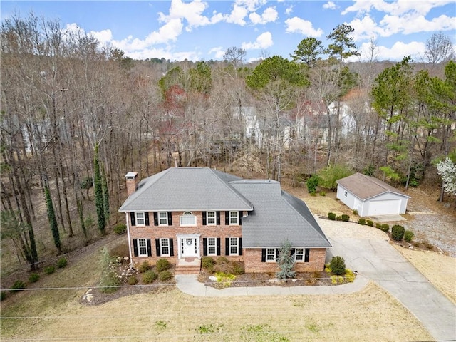 exterior space with an outdoor structure, concrete driveway, a garage, brick siding, and a chimney