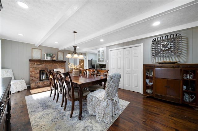 dining space with a notable chandelier, wood-type flooring, a textured ceiling, beamed ceiling, and a brick fireplace