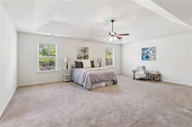 carpeted bedroom featuring a tray ceiling, multiple windows, and baseboards