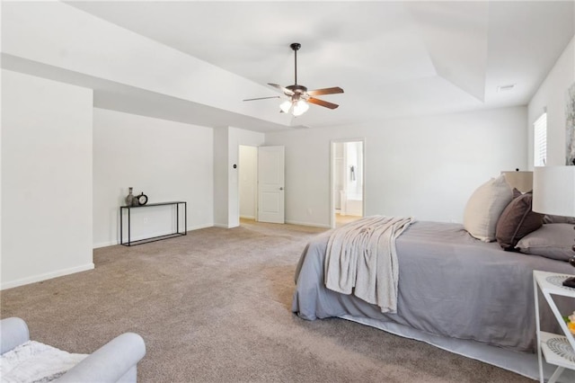 bedroom featuring ensuite bath, a raised ceiling, light colored carpet, and baseboards