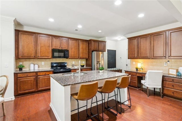 kitchen with dark wood-type flooring, an island with sink, light stone counters, black appliances, and a sink