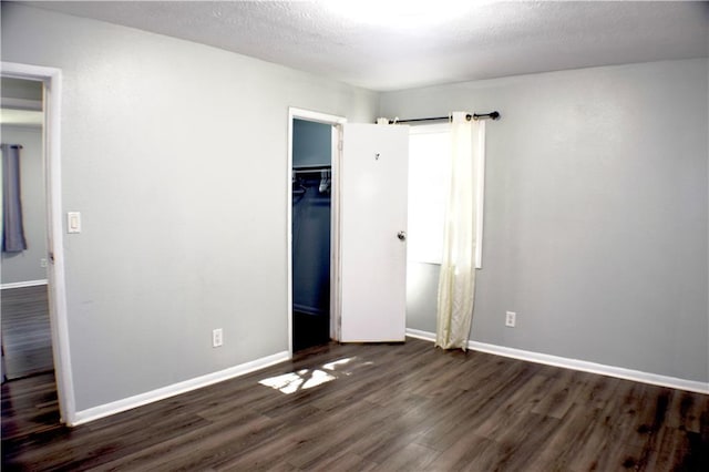 unfurnished bedroom with a textured ceiling, a spacious closet, dark hardwood / wood-style floors, and a closet