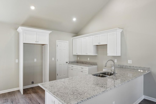 kitchen with a sink, white cabinets, light stone counters, and a peninsula