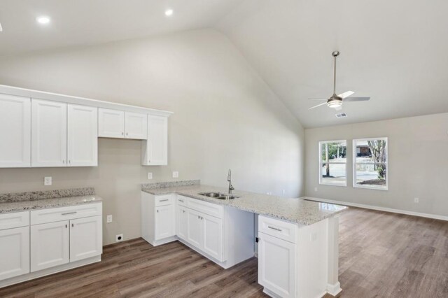 kitchen featuring a peninsula, light stone countertops, white cabinetry, and a sink