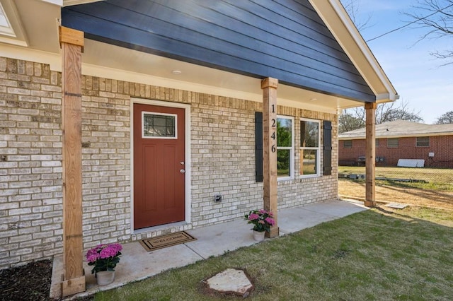 doorway to property featuring brick siding and a lawn