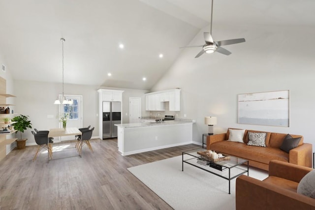 living area featuring ceiling fan with notable chandelier, high vaulted ceiling, light wood-type flooring, and baseboards