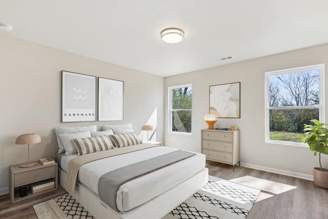 bedroom with baseboards, visible vents, and wood finished floors