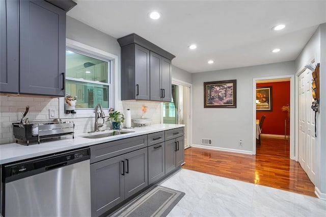 kitchen featuring sink, light wood-type flooring, gray cabinets, dishwasher, and backsplash