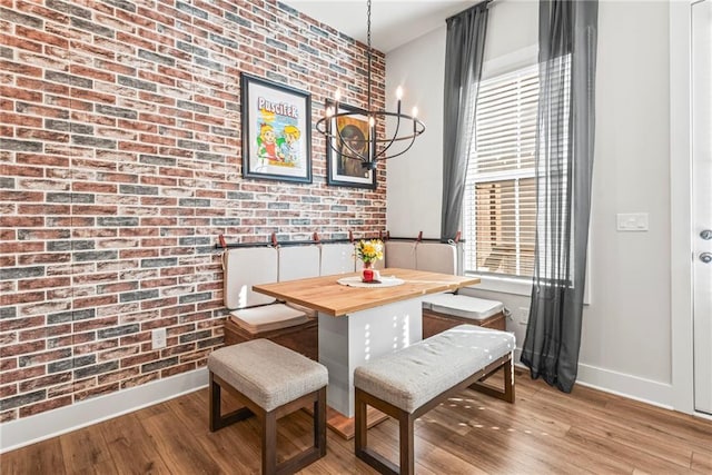 dining space with light hardwood / wood-style floors, brick wall, and a notable chandelier