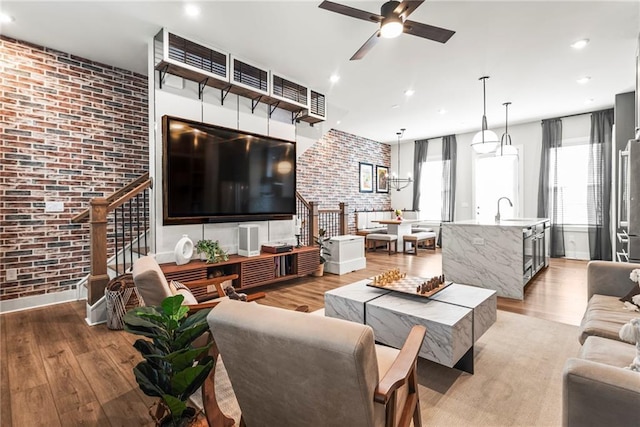 living room featuring sink, light hardwood / wood-style floors, ceiling fan, and brick wall