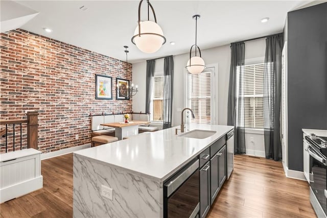 kitchen featuring brick wall, a kitchen island with sink, sink, decorative light fixtures, and stainless steel range oven