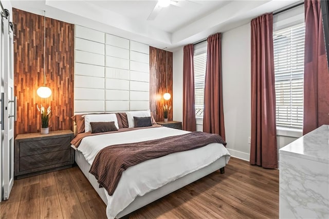 bedroom with multiple windows, a tray ceiling, ceiling fan, and dark wood-type flooring