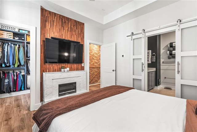 bedroom with connected bathroom, a barn door, light hardwood / wood-style flooring, a high end fireplace, and a closet