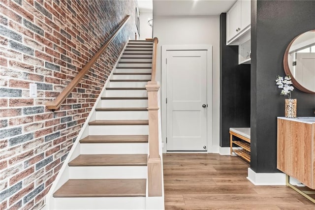 stairway with hardwood / wood-style flooring and brick wall