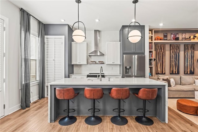 kitchen with sink, wall chimney range hood, a kitchen breakfast bar, stainless steel fridge, and decorative light fixtures