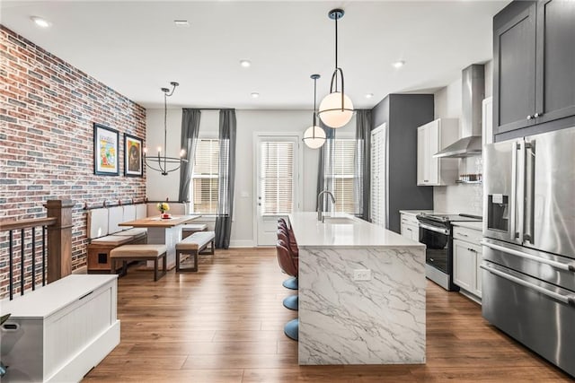 kitchen featuring sink, hanging light fixtures, wall chimney exhaust hood, stainless steel appliances, and brick wall