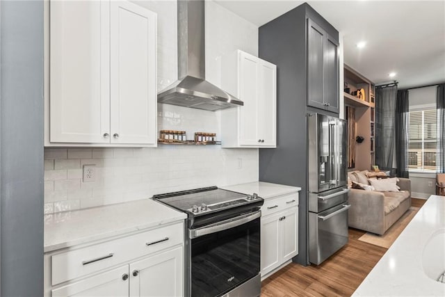 kitchen with wall chimney exhaust hood, light wood-type flooring, tasteful backsplash, white cabinetry, and stainless steel appliances