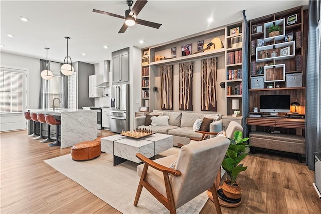 living room featuring ceiling fan, sink, light hardwood / wood-style floors, and built in features