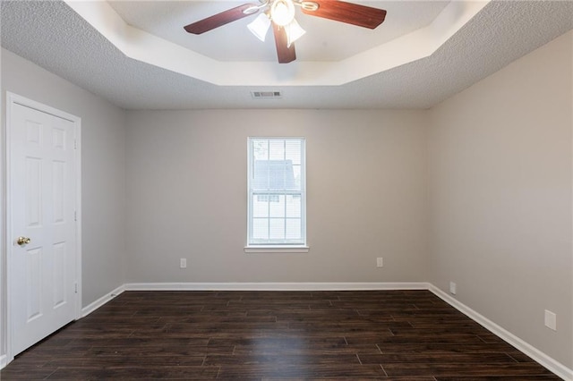 empty room featuring visible vents, baseboards, ceiling fan, dark wood-style floors, and a tray ceiling