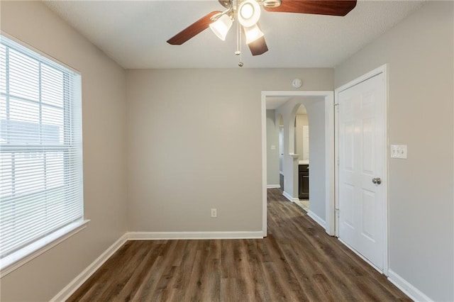 unfurnished room with arched walkways, ceiling fan, baseboards, and dark wood-style floors