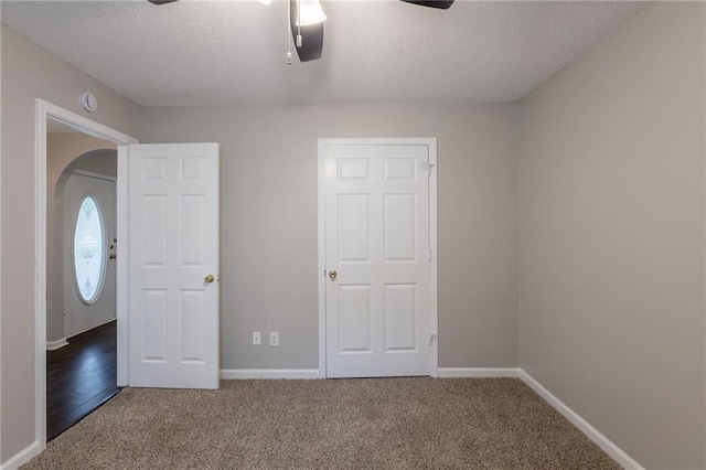unfurnished bedroom featuring arched walkways, baseboards, a textured ceiling, and carpet floors