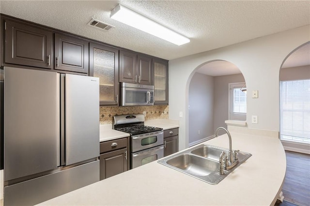kitchen with visible vents, glass insert cabinets, arched walkways, a sink, and stainless steel appliances