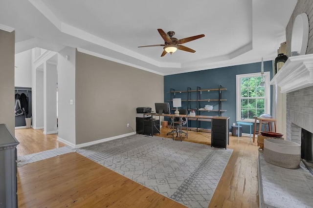 office area with a tray ceiling, ceiling fan, hardwood / wood-style floors, and a brick fireplace