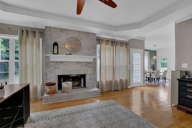 living room featuring a ceiling fan, wood finished floors, crown molding, and a brick fireplace