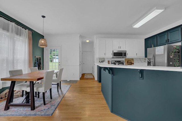 kitchen with stainless steel appliances, light countertops, a kitchen bar, hanging light fixtures, and white cabinets