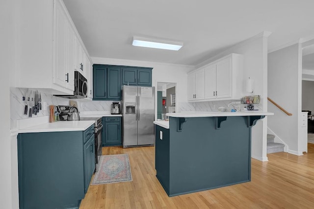 kitchen featuring appliances with stainless steel finishes, blue cabinetry, a breakfast bar, decorative backsplash, and light wood-style floors