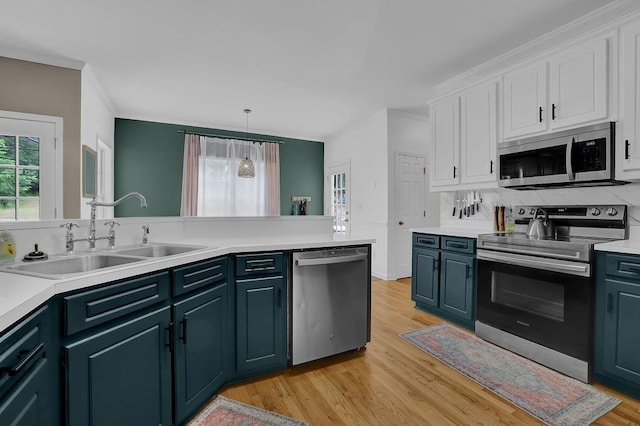 kitchen featuring appliances with stainless steel finishes, a sink, white cabinetry, light wood-type flooring, and crown molding