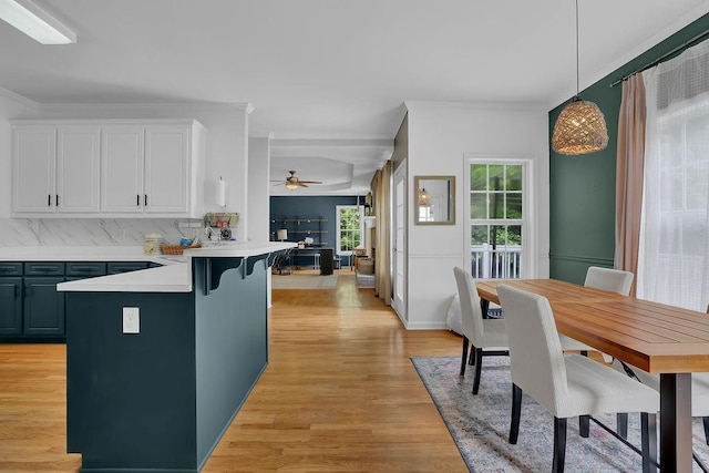 kitchen featuring white cabinetry, light countertops, a peninsula, light wood-style flooring, and ornamental molding