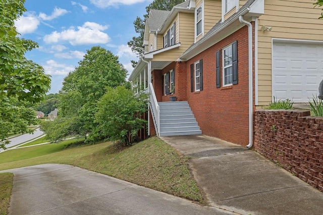 view of side of home featuring brick siding, a lawn, and stairs