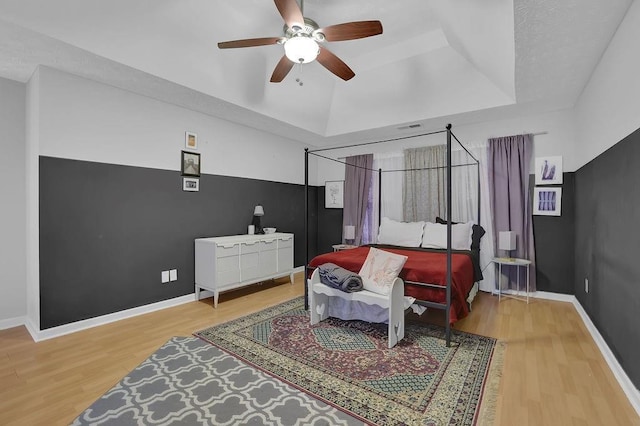 bedroom with a raised ceiling, wood finished floors, a ceiling fan, and baseboards